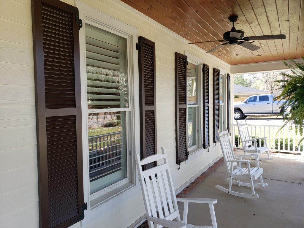 Dark brown louvered shutters along a covered porch with rocking chairs