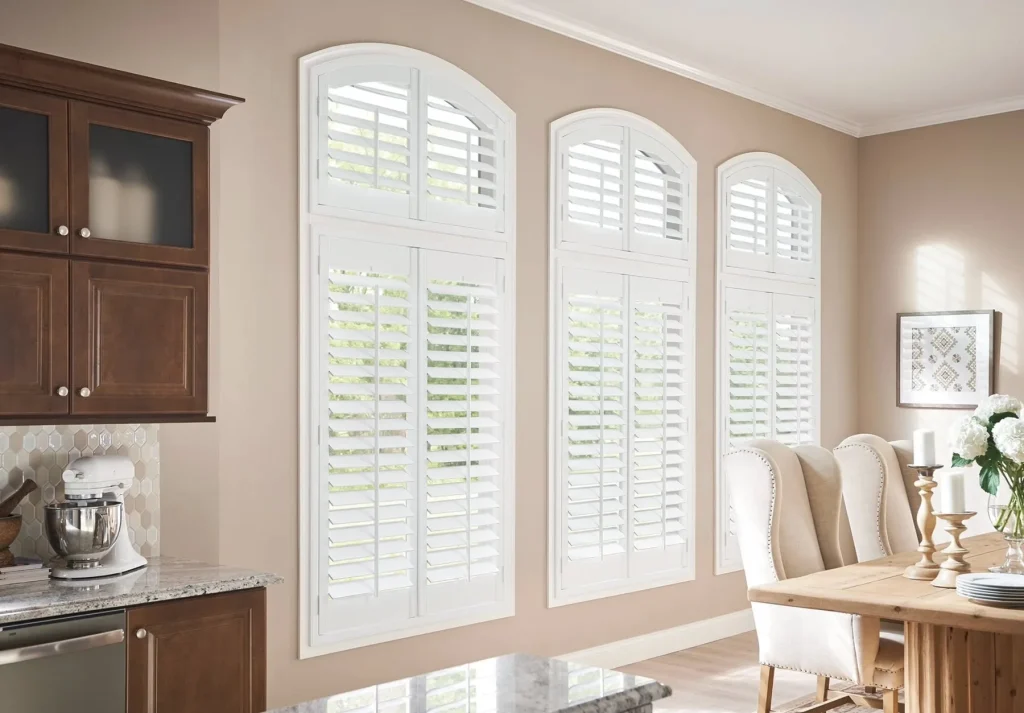 White arched plantation shutters on three windows in a dining area