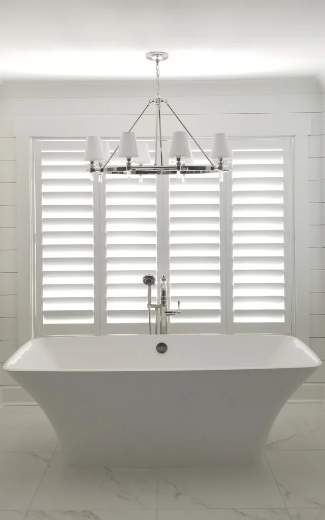 White plantation shutters framing a freestanding tub in a bright bathroom