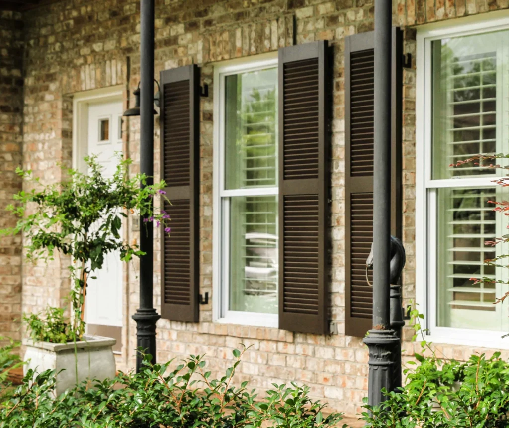 Brown louvered exterior shutters on the windows of a brick home