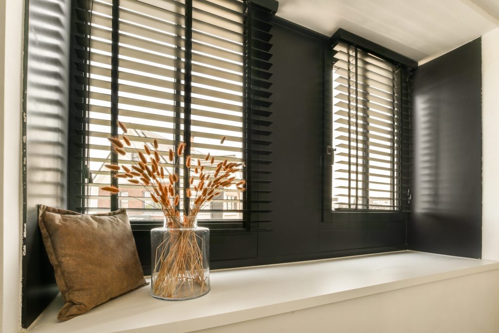 Some flowers in a vase on a window sie with black shutters and white trim around the windowsill