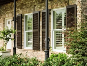 brick house with black exterior shutters on windows and white interior shutters, black columns